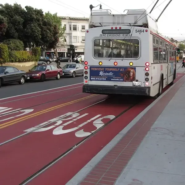 City street with a red coated transit lane and BUS lettering in front of a trolley bus